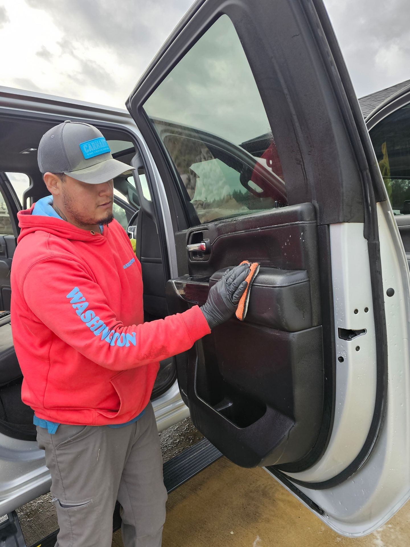 Person in red hoodie cleaning car door interior with a cloth.